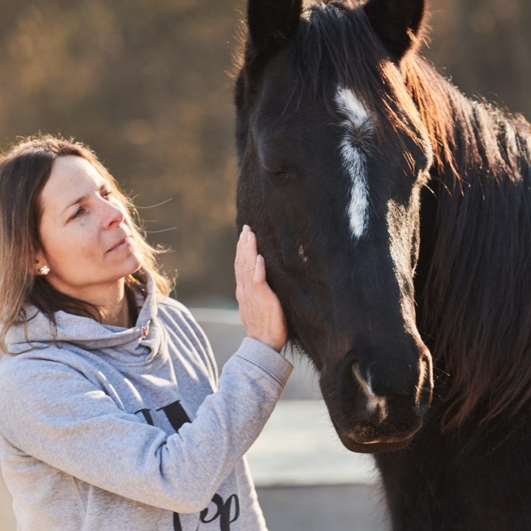 Eine Frau streichelt ein schwarzes Pferd mit sanfter Miene.